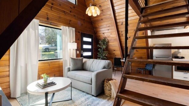 A cozy attic room with a sofa, a small table, and a staircase leading to a kitchen area.