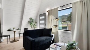 A modern living room with a black sofa, a round coffee table, a small side table, and a large window with curtains.
