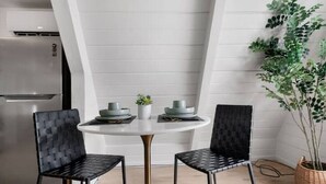 A modern kitchen with white cabinetry, a stainless steel refrigerator, and a round dining table with two black chairs.