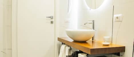 A modern bathroom with a large white sink, a wooden vanity, a black marble floor, and a white door.