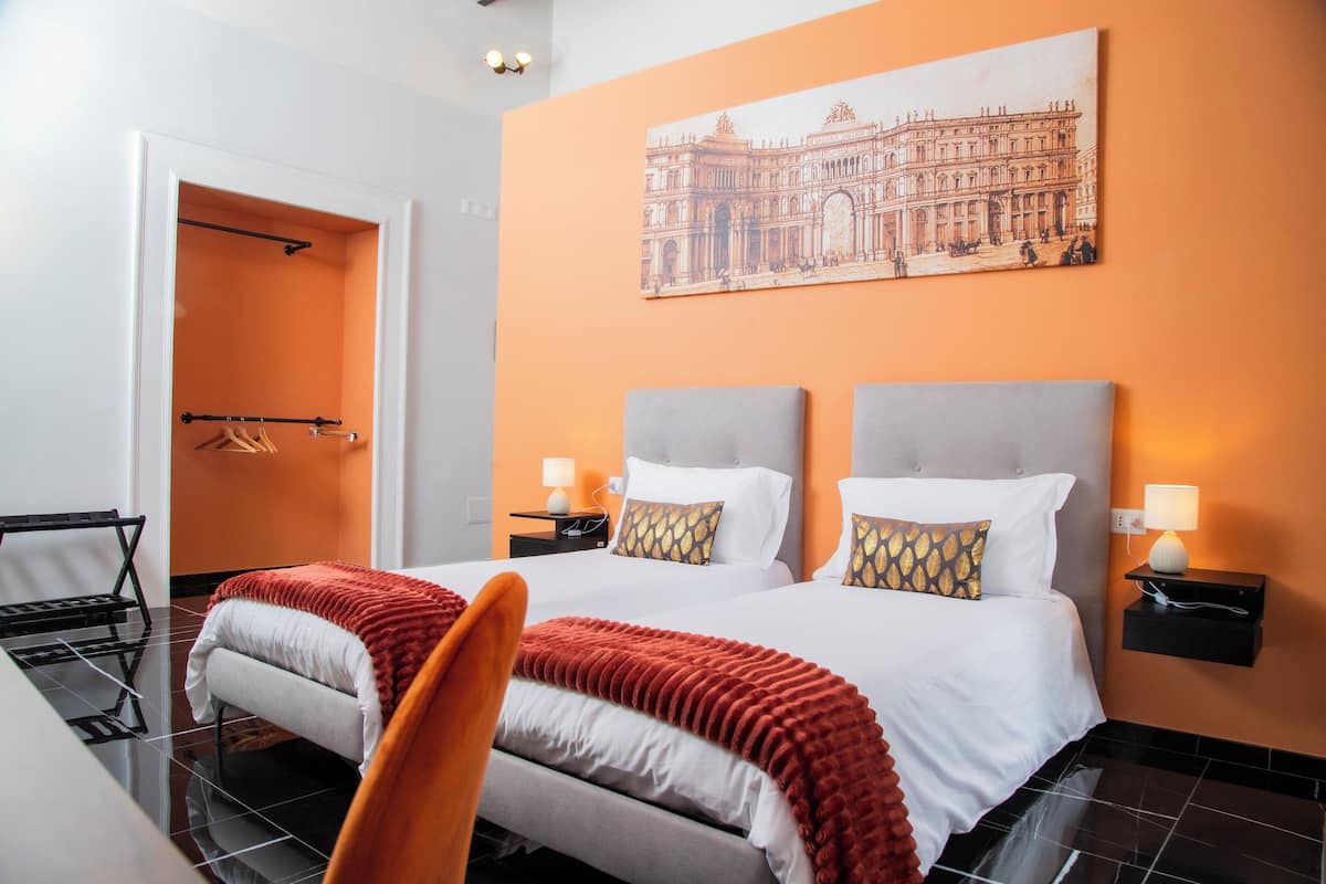 A hotel room with a double bed, two bedside tables with lamps, a chair, a desk, and a wardrobe.