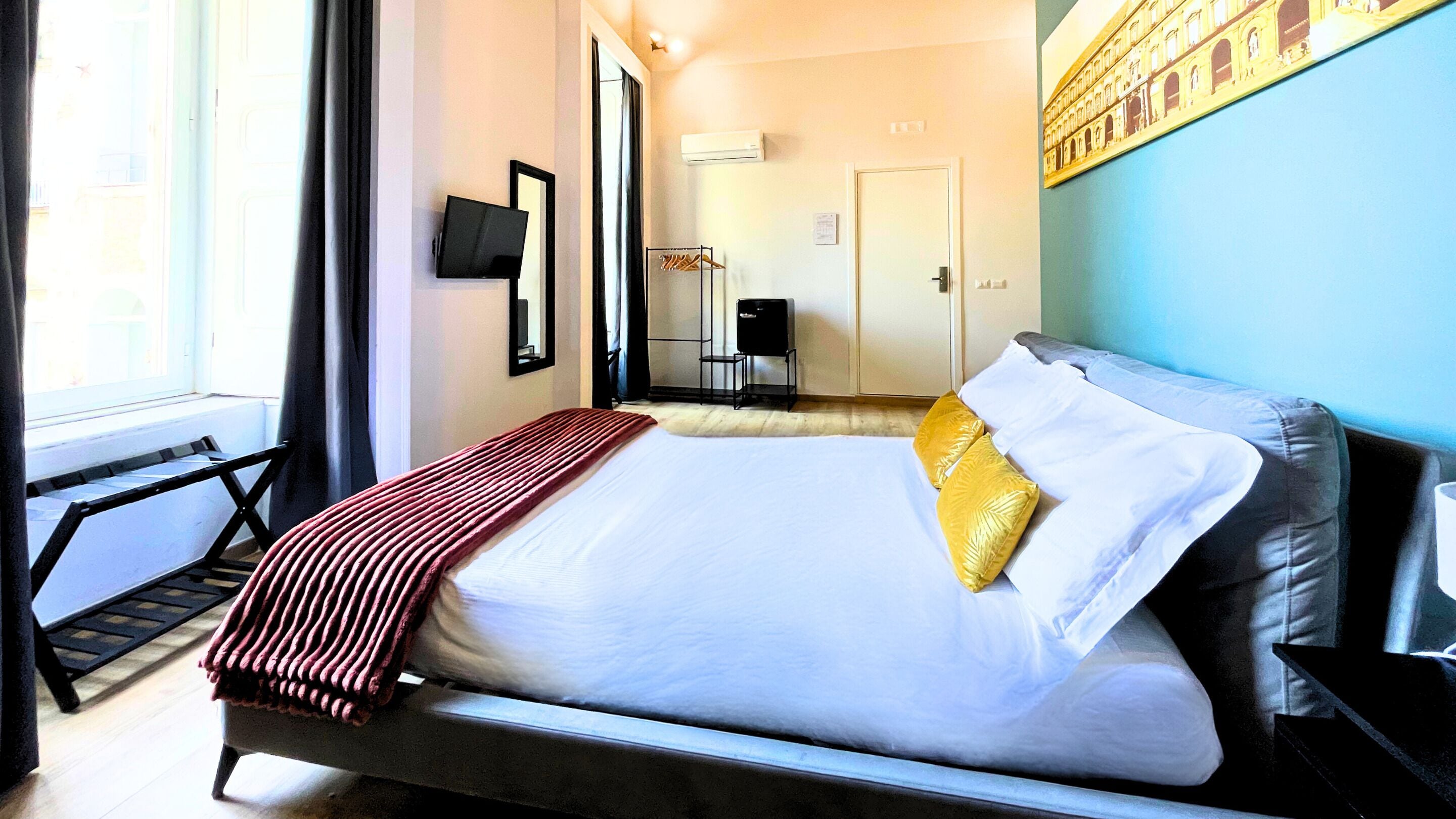 A hotel room with a bed, a TV, a wardrobe, and a window.