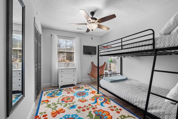 Una habitación con literas, ventilador de techo, televisor y una alfombra colorida.