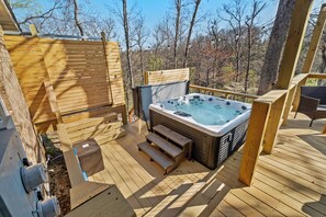 Una terraza de madera con un jacuzzi, escalones de madera y vistas a árboles.