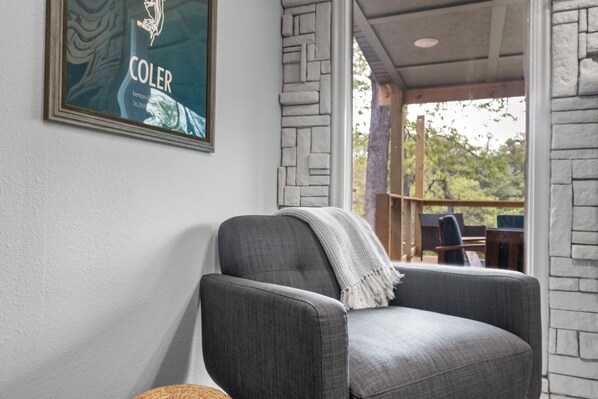 Un sillón gris con un plaid, un cuadro en la pared y vistas del exterior a través de una ventana.