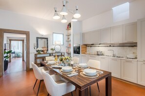 A modern kitchen with white cabinets, a wooden dining table set for six, and pendant lighting. - Georgia Penthouse in Lucca (Lucca)