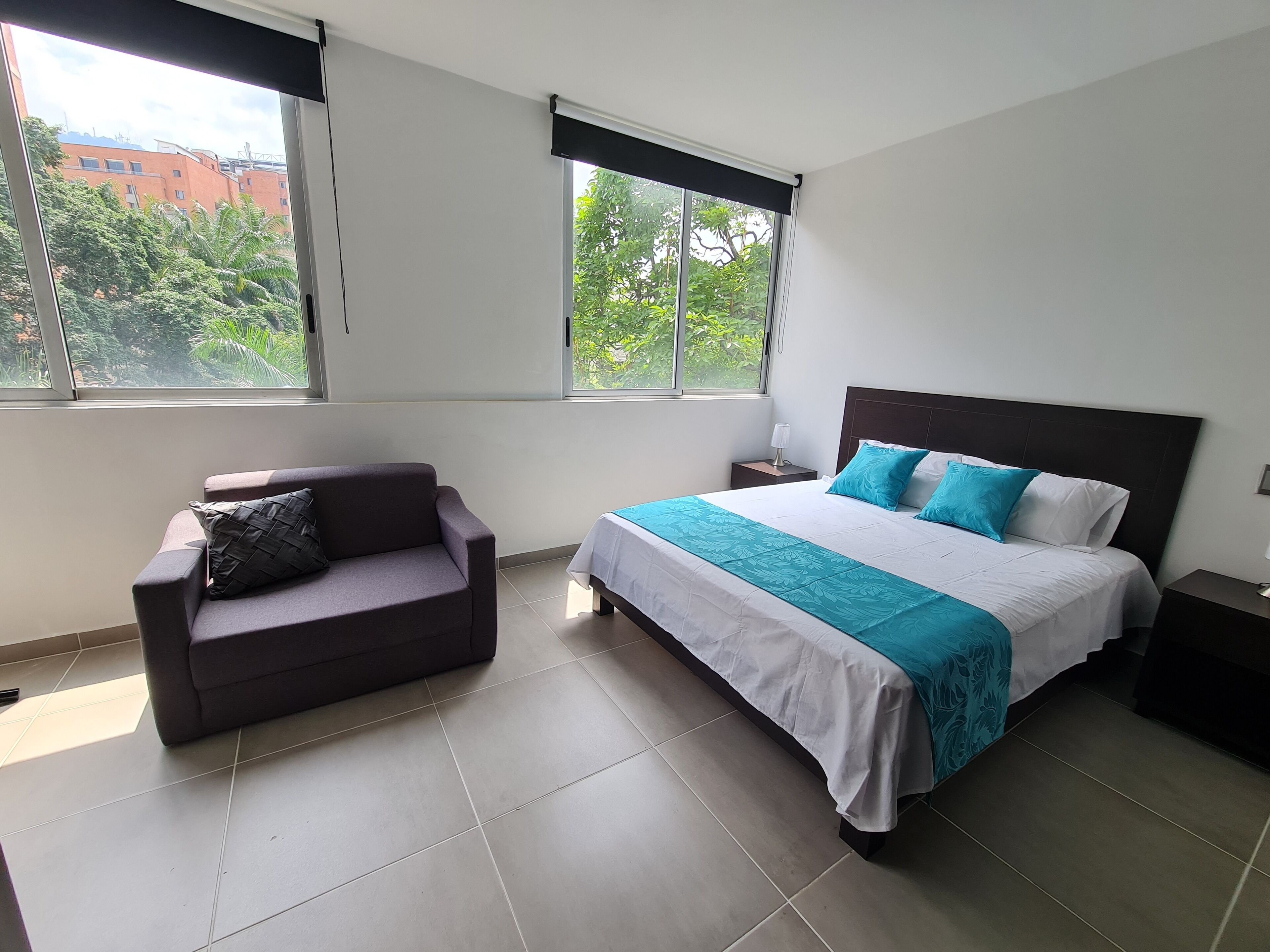 Une chambre à coucher avec un lit, une table de chevet, un canapé et de grandes fenêtres.