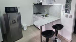 A compact kitchen with a microwave, gas stove, and two bar stools. - 403 Moderno Aparta-Suite en Versalles Tipo Loft - Cali Tower Suites & Lofts (Cali)