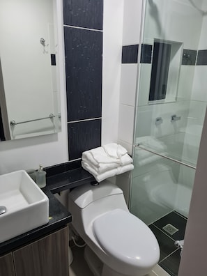Een moderne badkamer met een wit toilet, een glazen douchecabine en een zwart aanrecht.