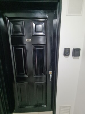 Een zwarte deur met het nummer 403, een keypad en een deurbel op een witte muur.