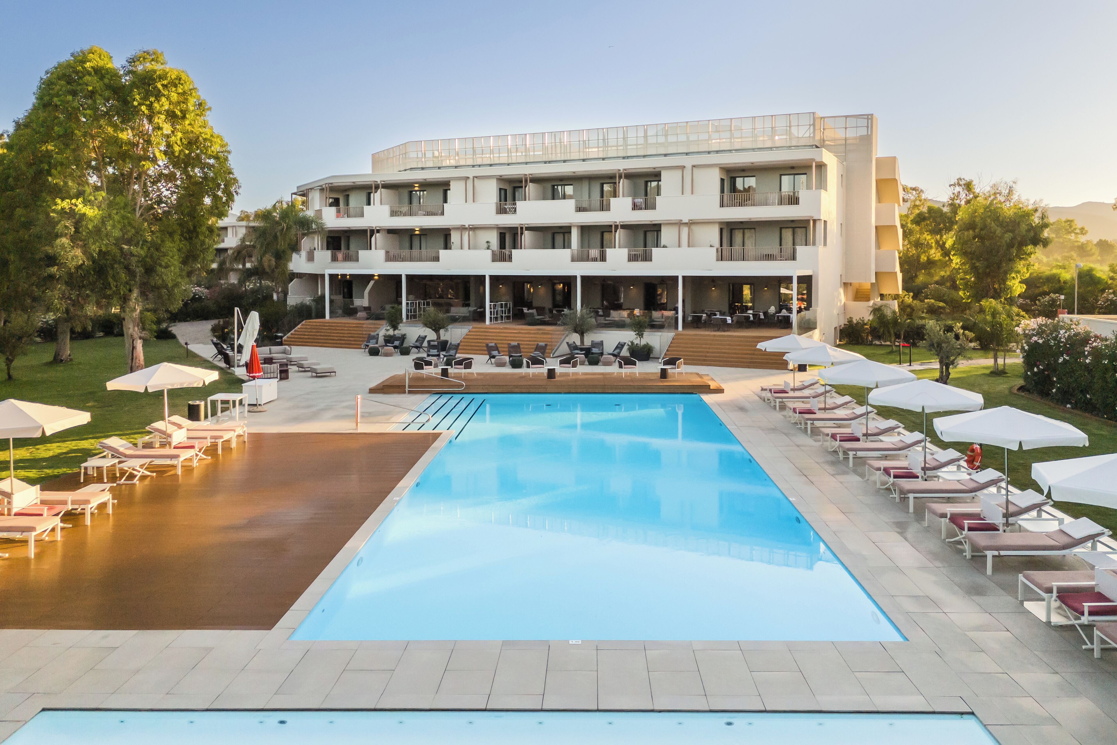 A modern hotel with a swimming pool, outdoor seating, and a well-maintained garden.