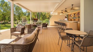 A covered outdoor patio with wicker furniture, a bar area, and a view of a lush garden. - VOI Tanka Selected (Villasimius)