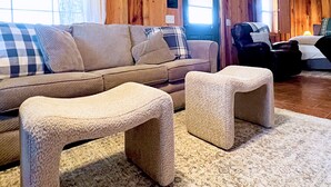Ein gemütliches Wohnzimmer mit einem beigen Sofa, zwei Poufs und einer Holzvertäfelung.