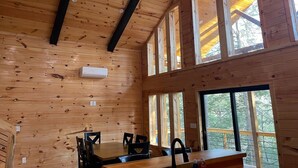 A wooden cabin interior with a dining table, chairs, and large windows. - Unwind at Whispering Woods / Hot Tub, Waterfall, Arcade & Nature (camton)