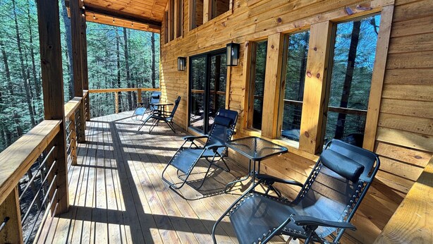 A wooden deck with outdoor seating and large windows overlooking a forest. - Unwind at Whispering Woods / Hot Tub, Waterfall, Arcade & Nature (camton)