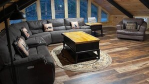 A cozy loft-style room with a large sectional sofa, a wooden coffee table, and a leather armchair. - Unwind at Whispering Woods / Hot Tub, Waterfall, Arcade & Nature (camton)