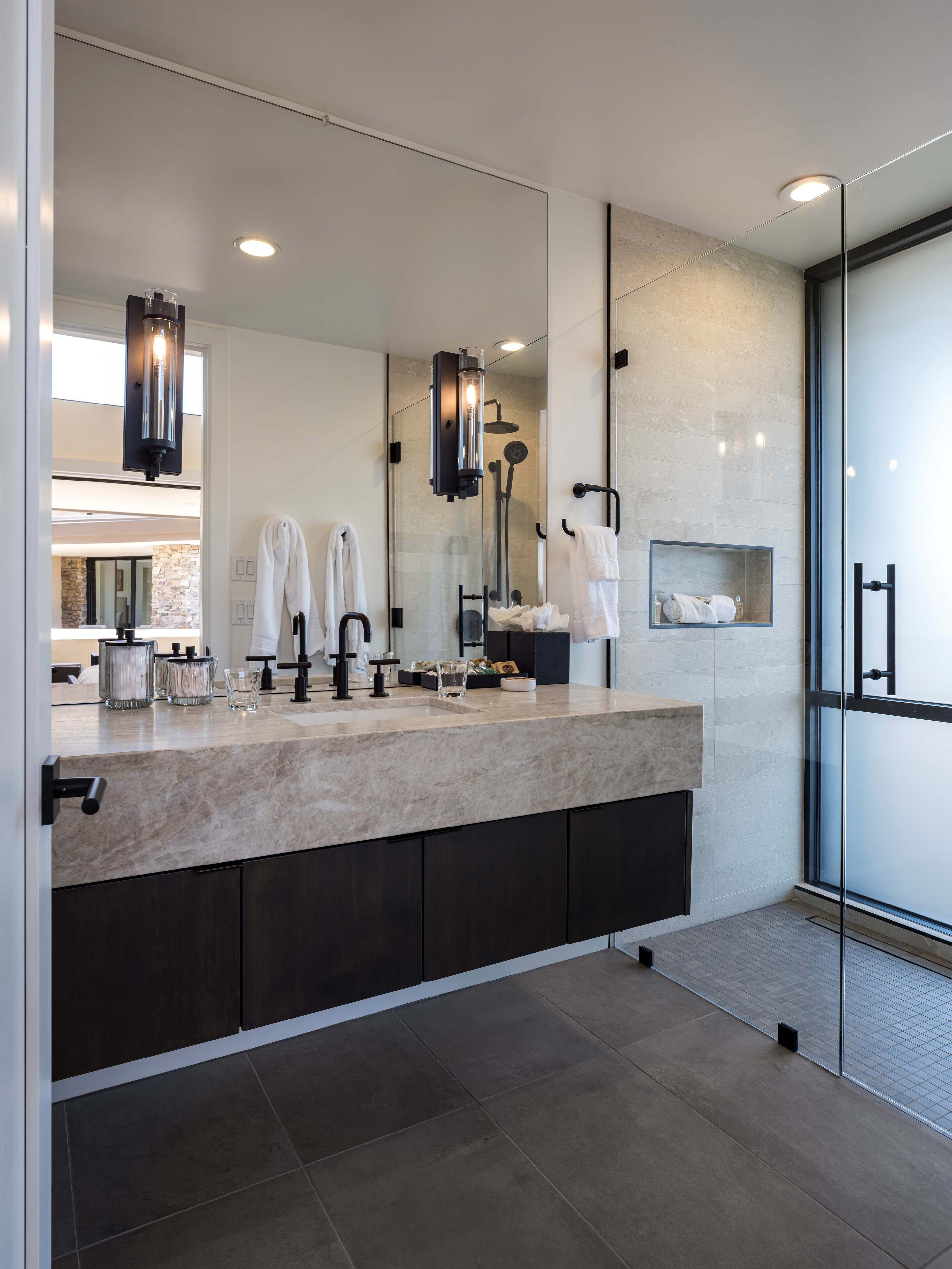 A modern bathroom with a large mirror, dark cabinets, and a glass shower enclosure.