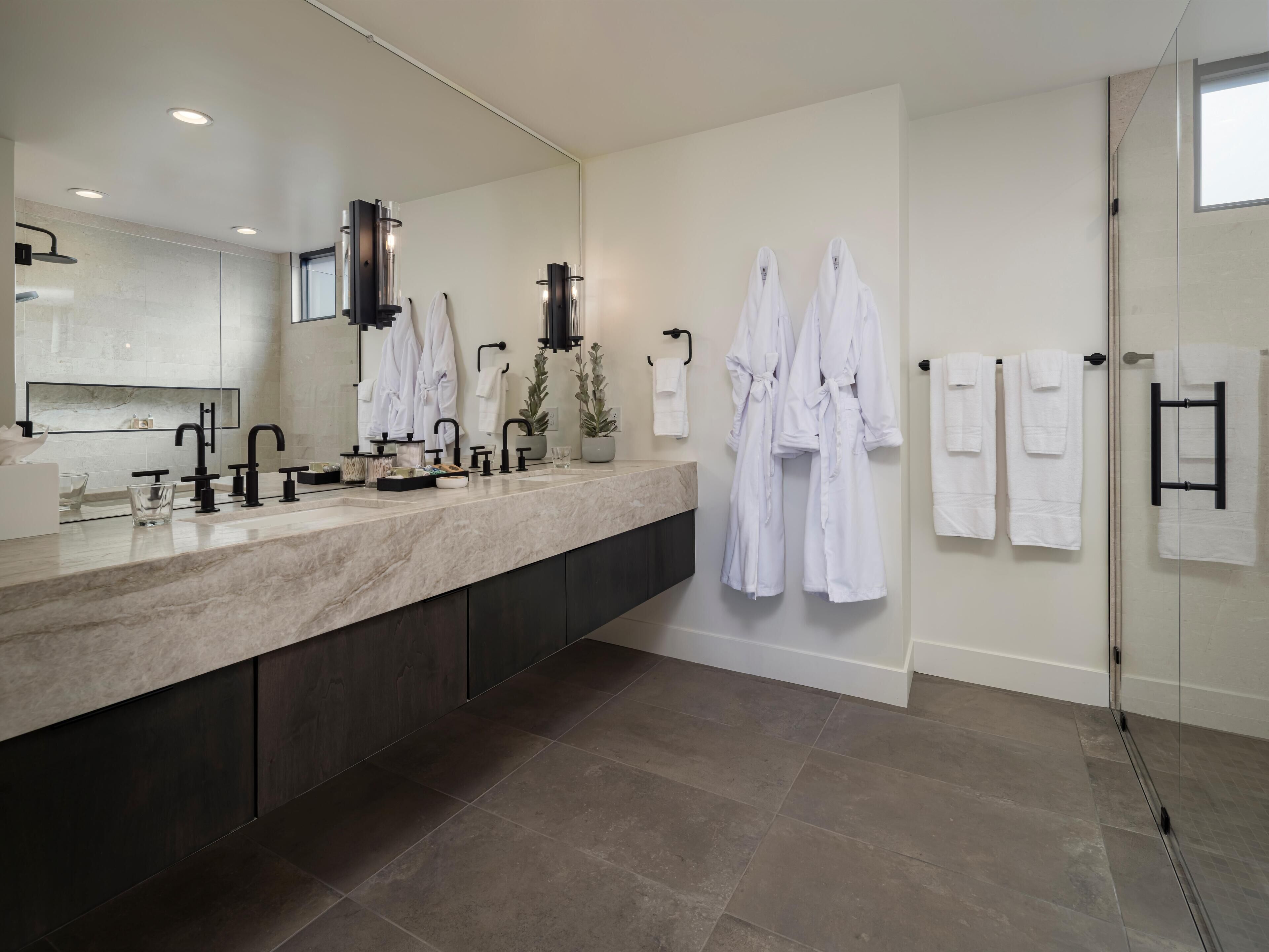 A modern bathroom with a large mirror, a marble countertop, and multiple white towels.