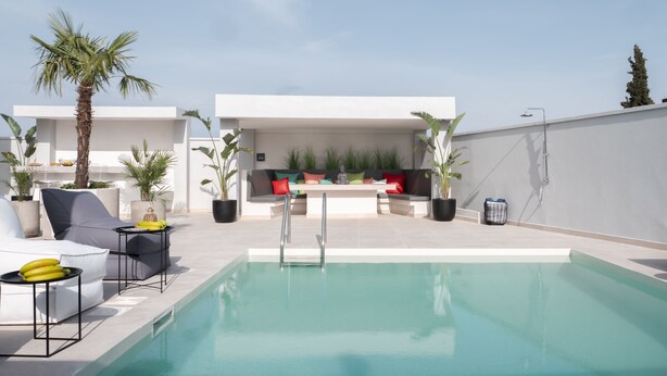 Un espace piscine extérieur moderne, aménagé avec des sièges, une statue et des plantes en pot.
