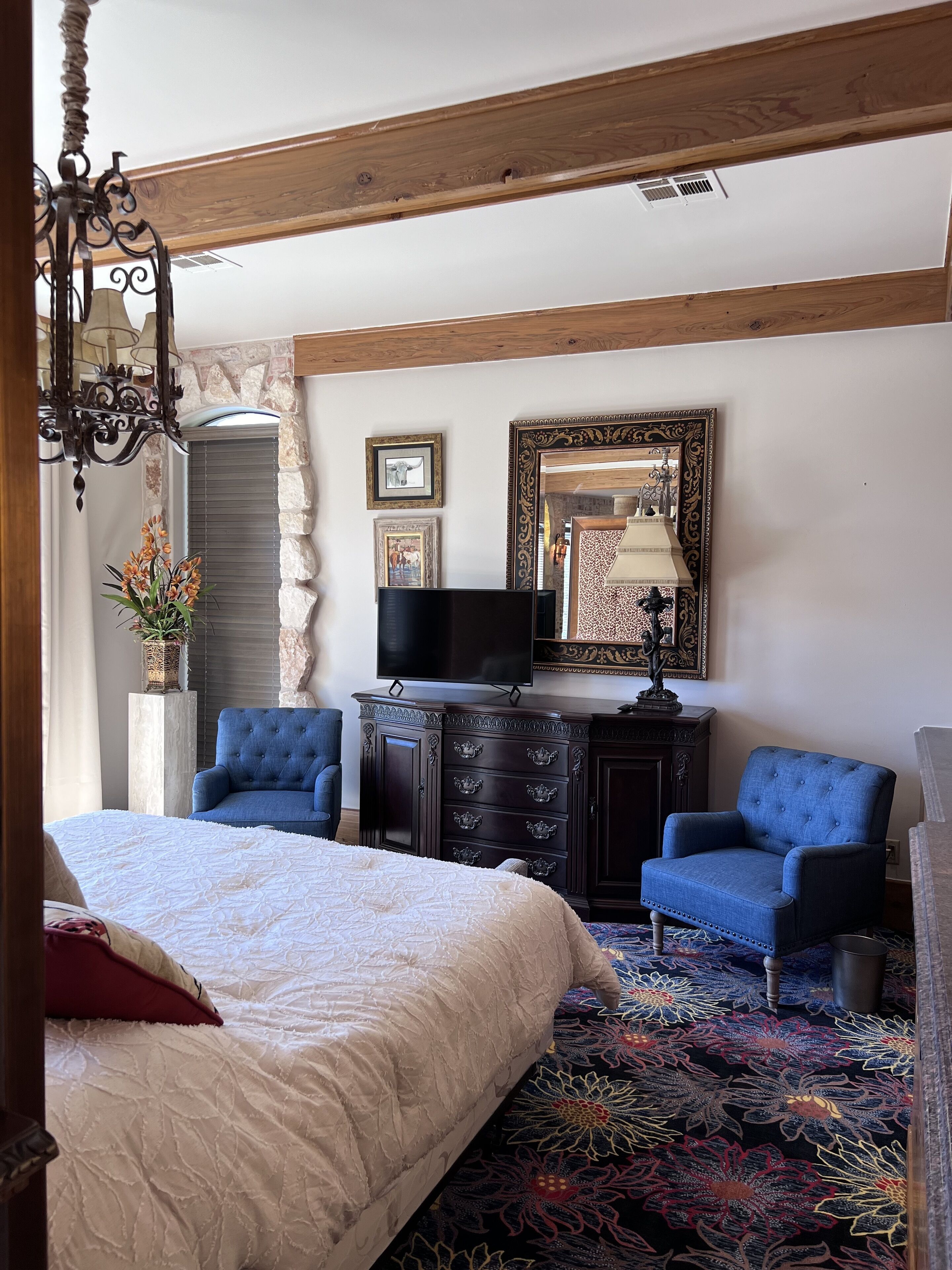 Un dormitorio con una cama grande, un aparador, dos sillones, un televisor y un espejo.