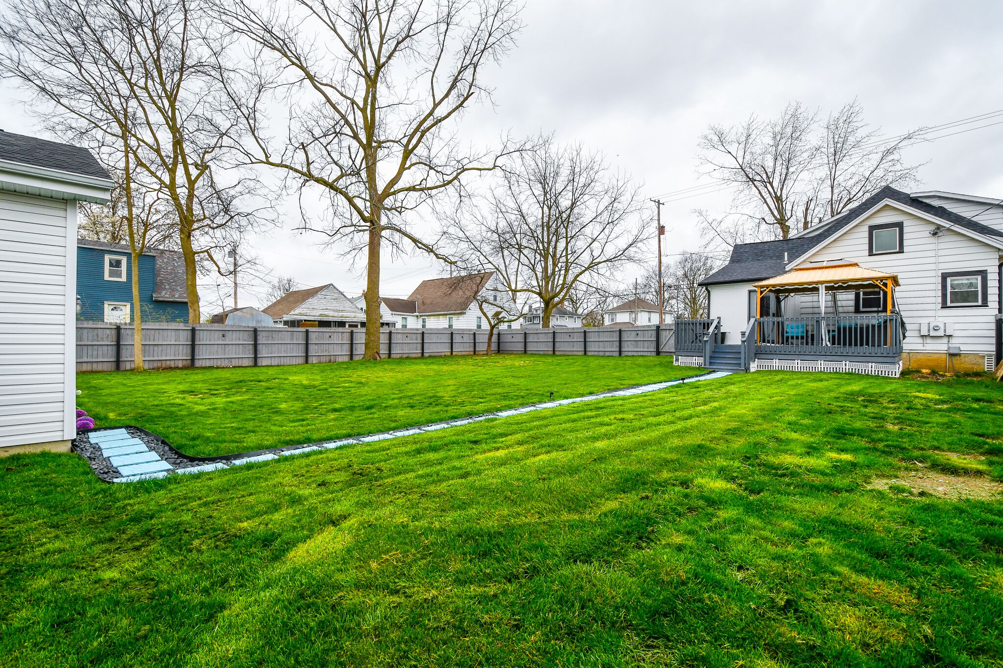 A backyard with a well-maintained lawn, a wooden deck, and a house with a porch.