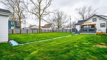A backyard with a well-maintained lawn, a wooden deck, and a house with a porch.