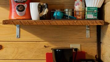 Een keuken met houten kastjes, een koffiezetapparaat, een koffiekan, een mok, een blik Dunkin' koffie, een potje room en een doos papieren bekertjes.