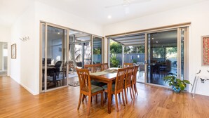 Comedor con mesa y sillas de madera, una silla colgante y vista al patio trasero a través de puertas de vidrio.