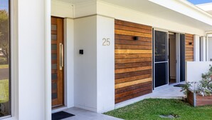 Una casa moderna con fachada de madera, el número '25' en la pared y un gran ventanal corredizo.