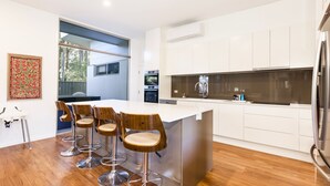 Una cocina moderna con una isla central, taburetes de bar, horno empotrado y un amplio ventanal.