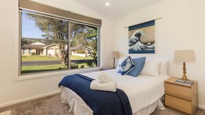 Un dormitorio con un ventanal grande, una cama con manta azul, una obra de arte en la pared y lámparas de noche.