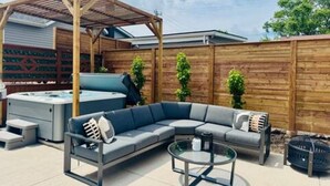A patio with a wooden pergola, a hot tub, a sectional sofa, and a glass table.