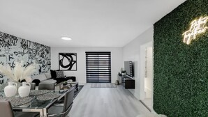 A modern living room with a black and white abstract wall art, a green wall with a neon sign, and a minimalist furniture arrangement.