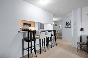 A modern kitchen with a central island, bar stools, and a dining area with a table and chairs. - Whistling Peaks | Hot Tub | Pool | Gas Fireplace (Radium Hot Springs)