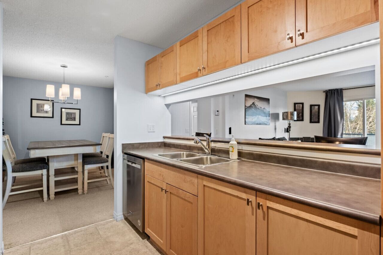 A modern kitchen with wooden cabinets, a stainless steel sink, and a dining area with a table and chairs.