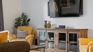 Una sala de estar moderna con un televisor de pantalla plana grande montado en la pared, un mueble de madera con puertas de vidrio y un sillón amarillo.