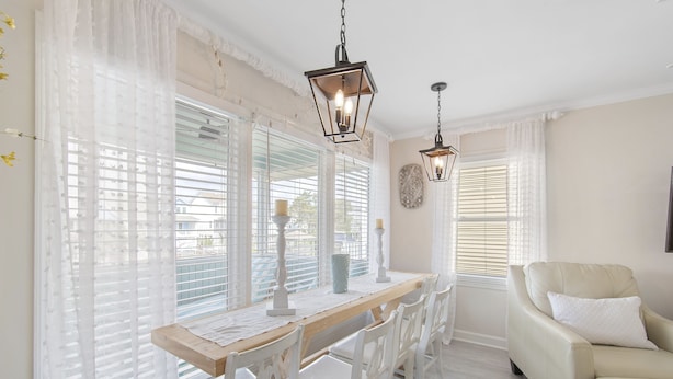A dining area with a wooden table and white chairs, a beige sofa, and two hanging lanterns. - Beach House - Private Dock + Walk to the Beach (Holden Beach)