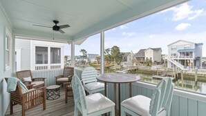 A covered outdoor seating area with wooden chairs and a table, overlooking a waterway with houses and docks. - Beach House - Private Dock + Walk to the Beach (Holden Beach)