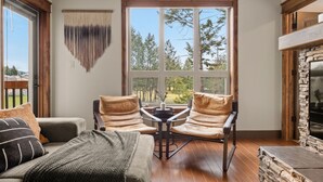 Una sala de estar acogedora con chimenea, un ventanal con vistas a árboles y un rincón de estar cómodo con una mesita de centro.
