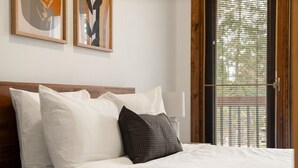 Una cama bien hecha con almohadas blancas y oscuras, un cabecero de madera y una ventana con persianas.