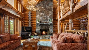 A log cabin interior with a stone fireplace, wooden furniture, and a piano.