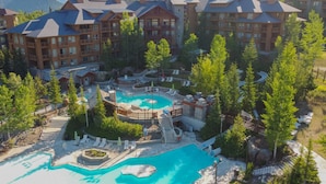 A resort with multiple buildings, a central pool area with a hot tub, and a mountain backdrop.