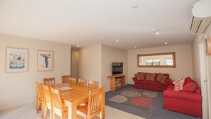 Ein Wohnzimmer mit einem roten Sofa, einem Holzespeisetisch mit Stühlen, einem Fernseher und Bildern an den Wänden.