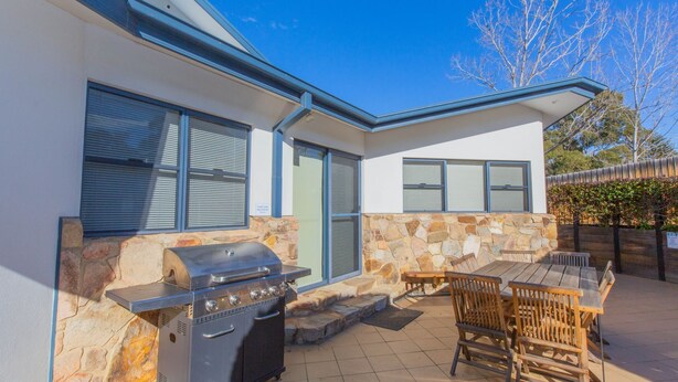Ein modernes Haus mit Natursteinaußenwand, Grill und Terrasse mit Holzmöbeln.