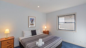 Une chambre d’hôtel avec un lit, une table de chevet, une lampe, une fenêtre et un tableau encadré au mur.