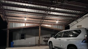 En vit SUV står parkerad i ett garage med tak och väggar, där taket är av metall och väggarna har träbjälkar.