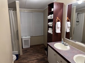 Une salle de bain avec un meuble-lavabo en bois, un grand miroir, une douche et un panier à linge.