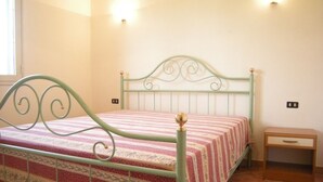 Una cama con estructura metálica y una colcha estampada, una mesita de noche y un enchufe en la pared.