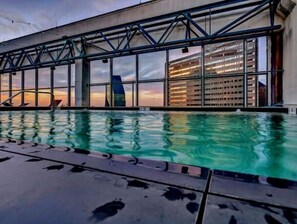 A swimming pool with a modern architectural backdrop, large windows, and a clear view of the sky. - Luxury Apt w/Parking CityView/Pool/Gym/PoolTable (Dallas)