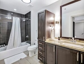 A modern bathroom with a bathtub, toilet, and dark wooden cabinets. - Luxury Apt w/Parking CityView/Pool/Gym/PoolTable (Dallas)